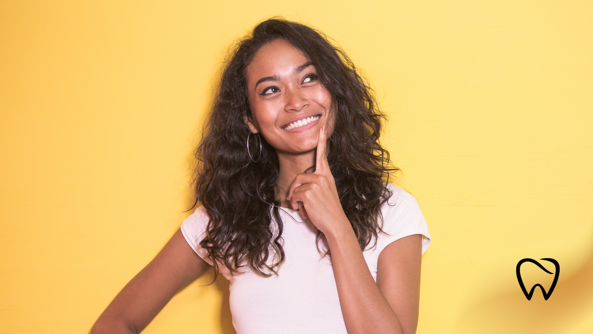 Woman with curly hair, smiling while touching her chin, yellow background.