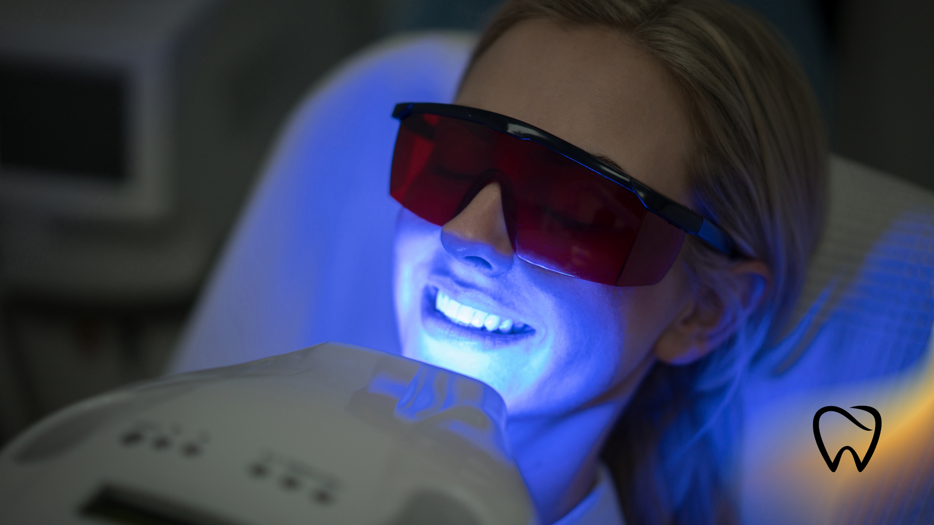 Woman undergoing teeth whitening treatment, wearing protective glasses, under blue light.