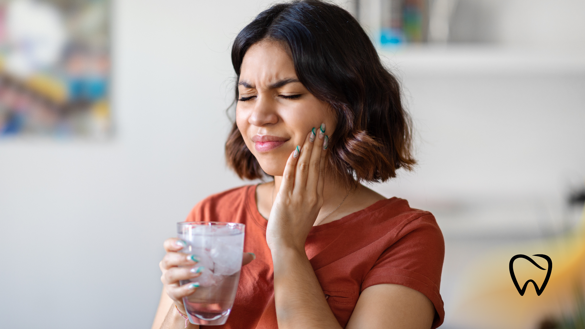 Woman with toothache holds face and glass of water; indoors.