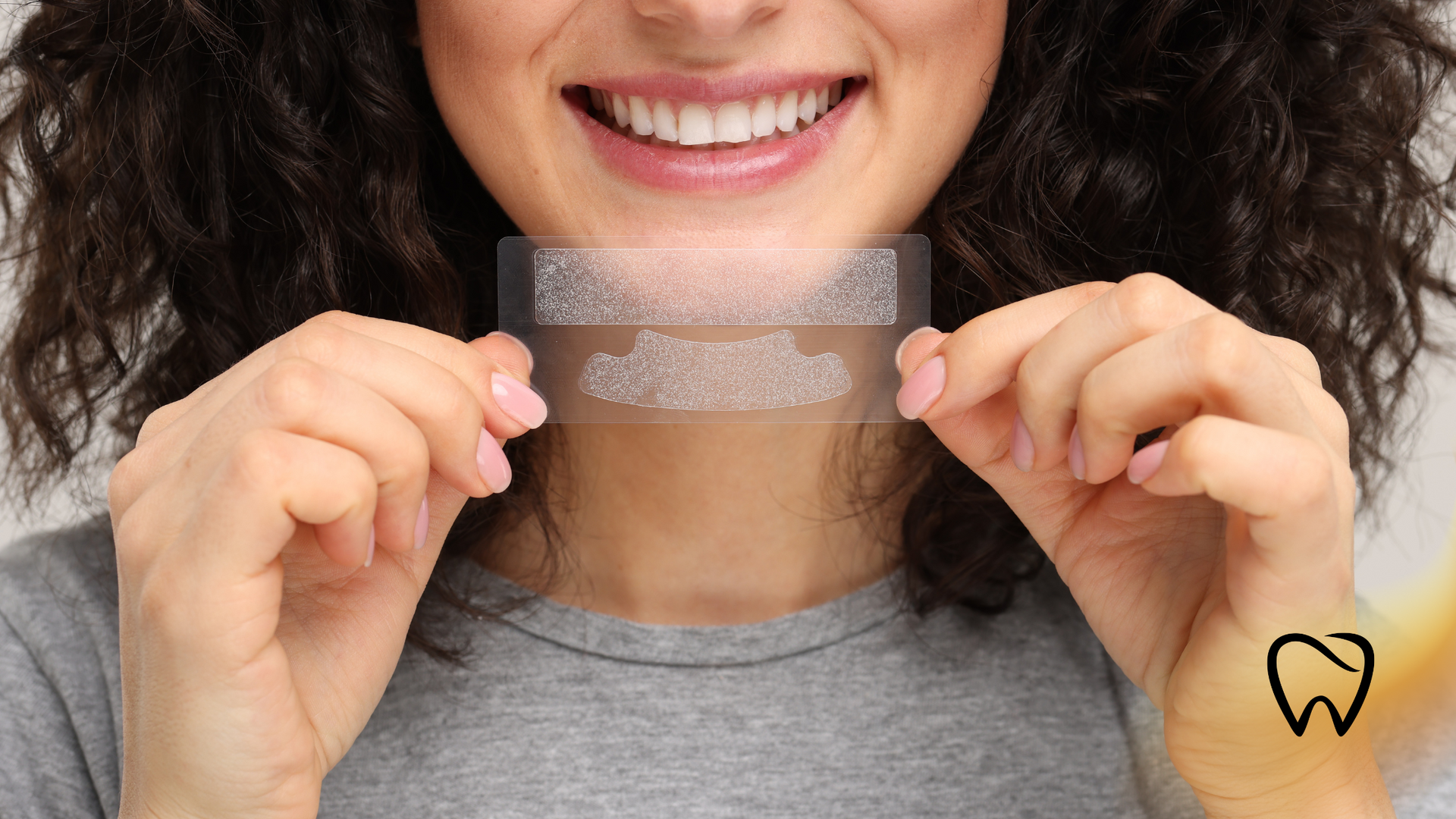 Woman holding teeth whitening strips, smiling with bright white teeth.