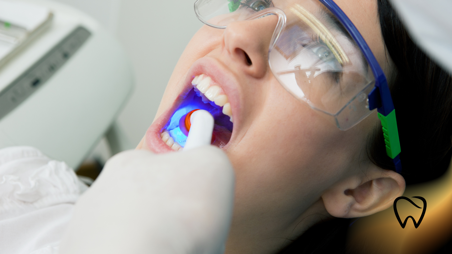 Dentist shining blue light into a patient's open mouth during a dental procedure.