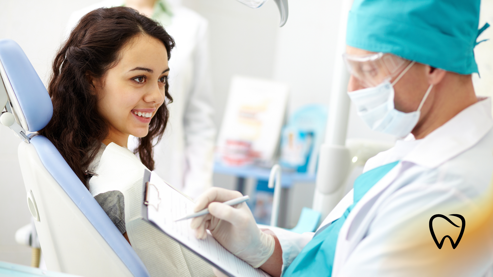 Woman smiling in a dentist chair; dentist in mask and gloves reviews paperwork.