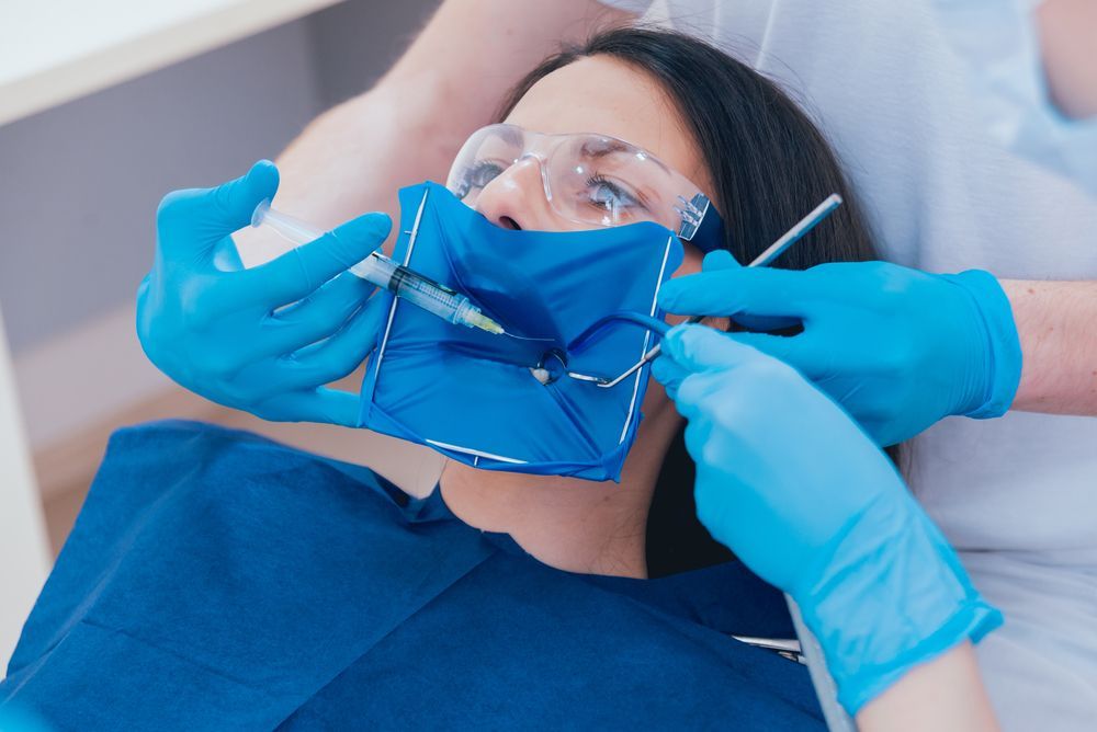 Woman in dentist chair with blue dental dam, gloves, and tools.