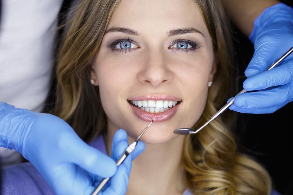 Woman at the dentist, smiling while dental tools are used to check her teeth.