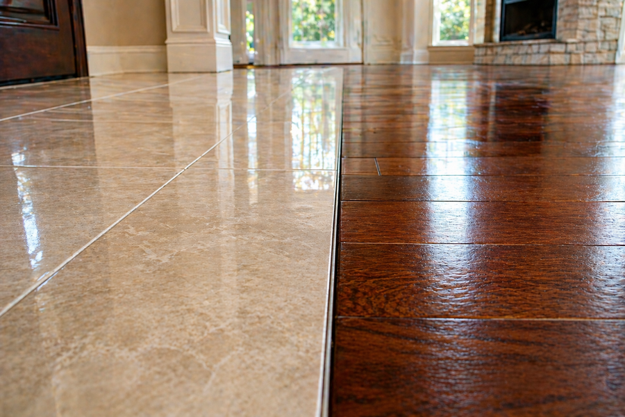 Shiny tiled floor with a visible seam between light beige and dark brown sections, reflecting a room and doorway