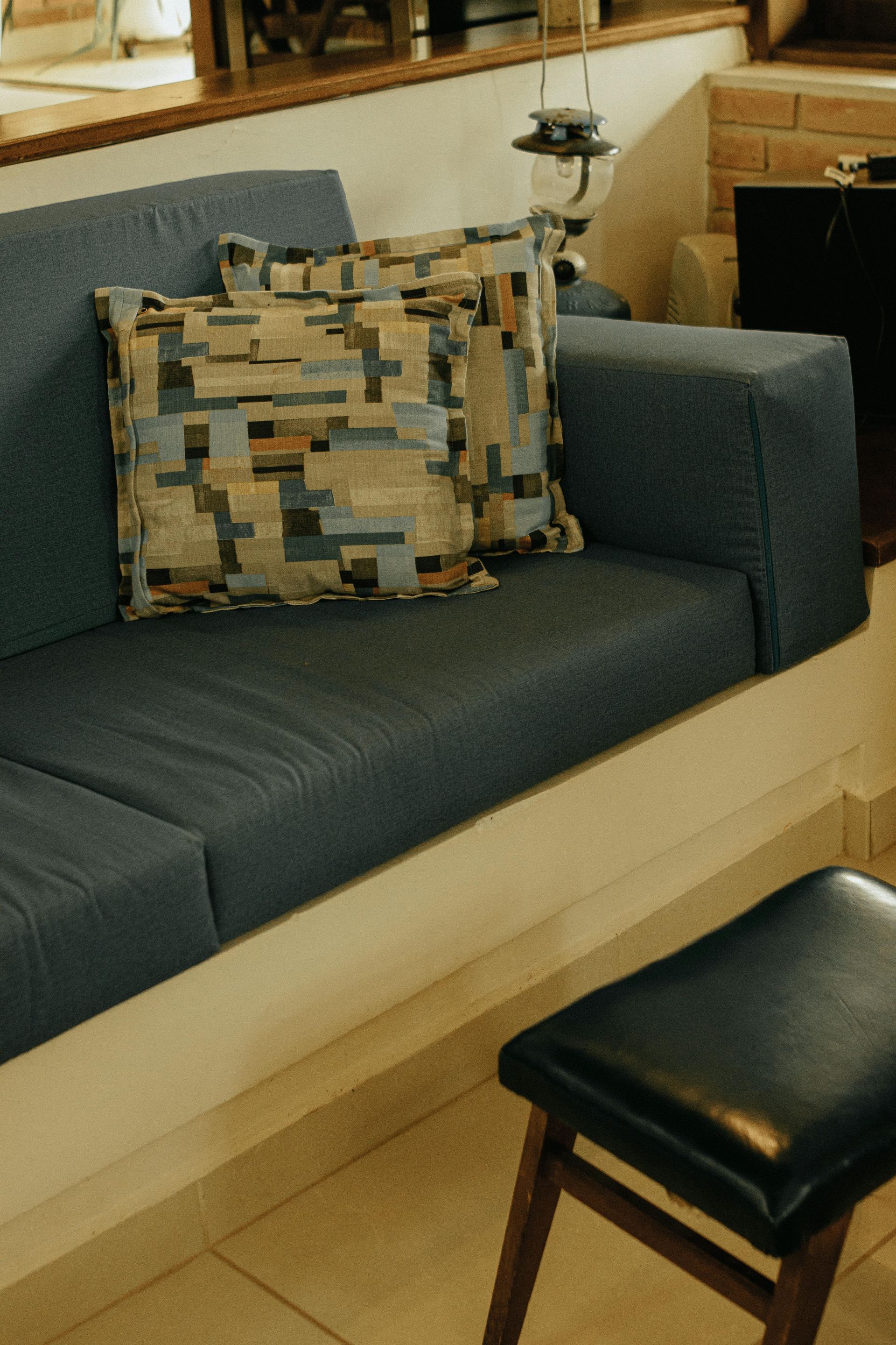 Blue-gray couch with patterned pillow and black ottoman in a living room-style setting