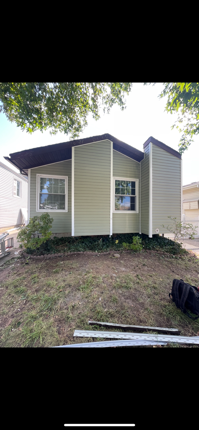 A small house with a lot of windows is sitting on top of a grassy hill.