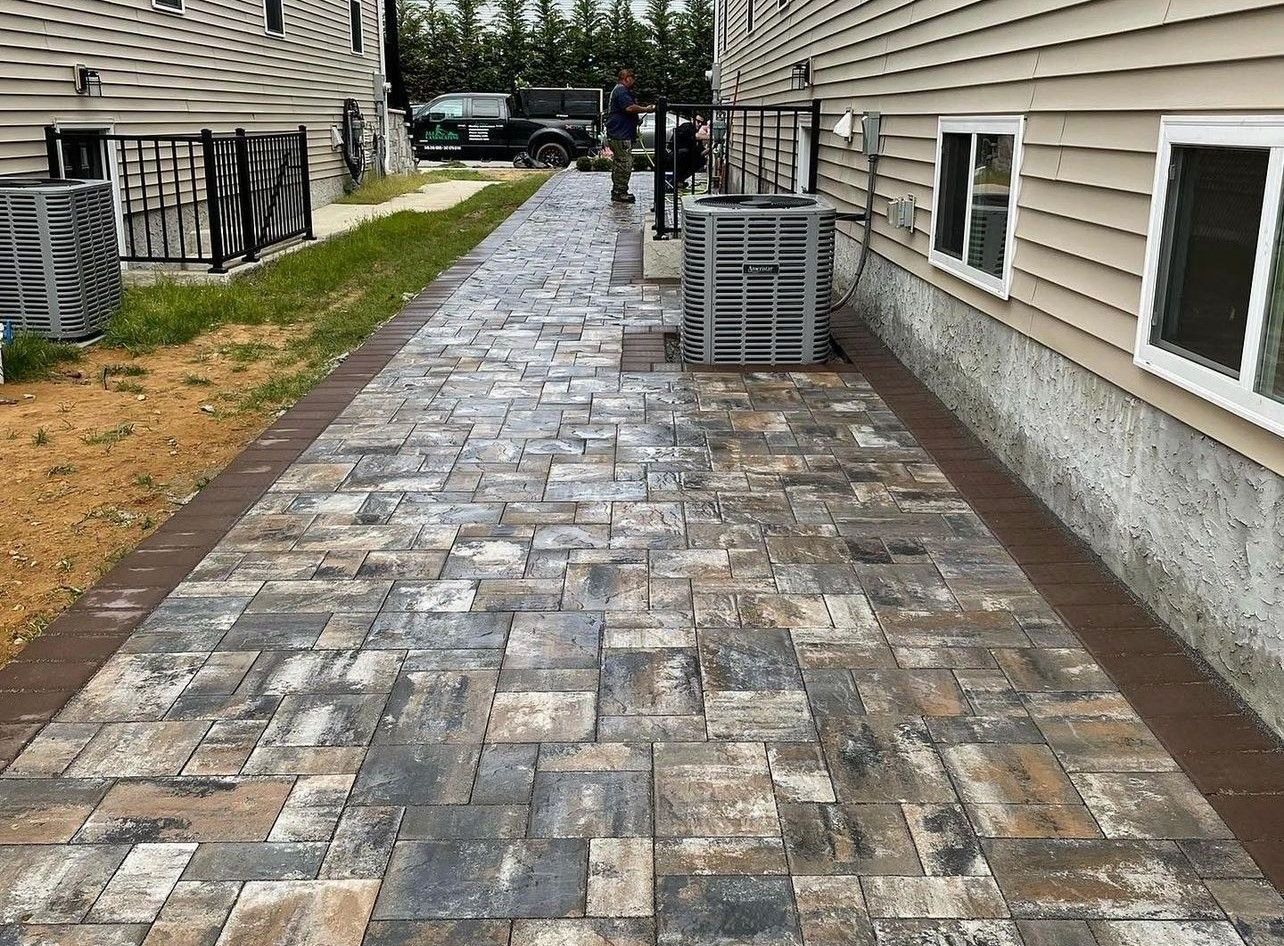 A brick walkway leading to a house with an air conditioner.