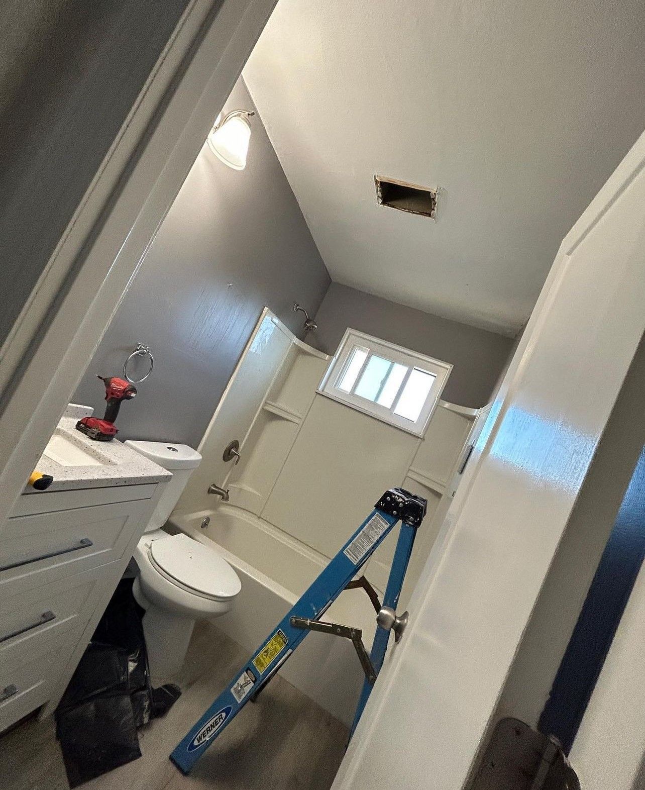 A bathroom with a toilet , bathtub , sink and ladder.