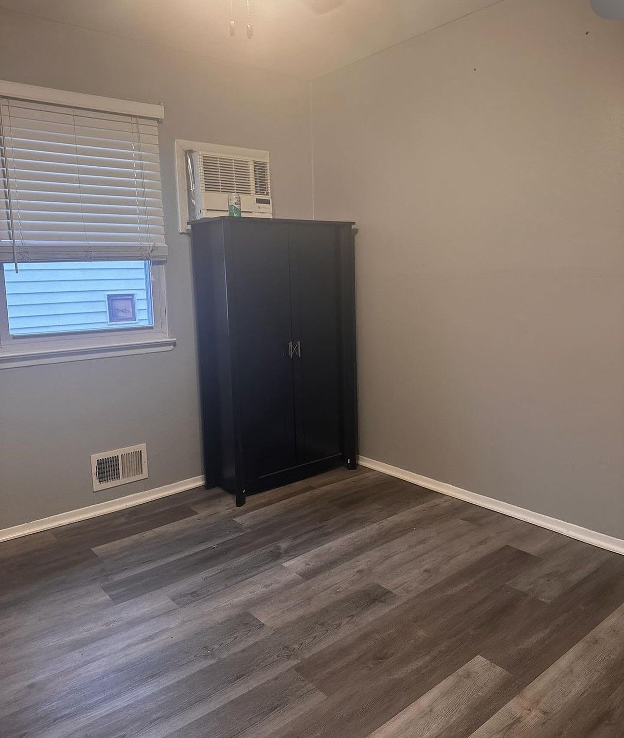 A bedroom with hardwood floors and a window with blinds.