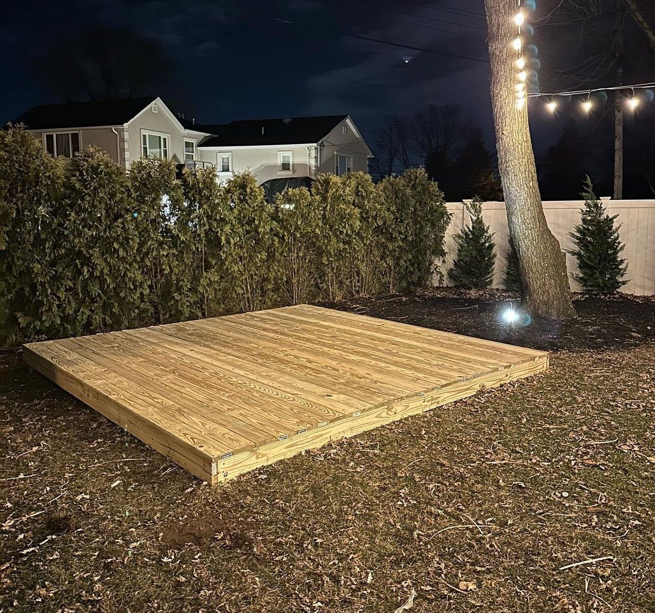 A wooden platform is sitting in the middle of a yard at night.