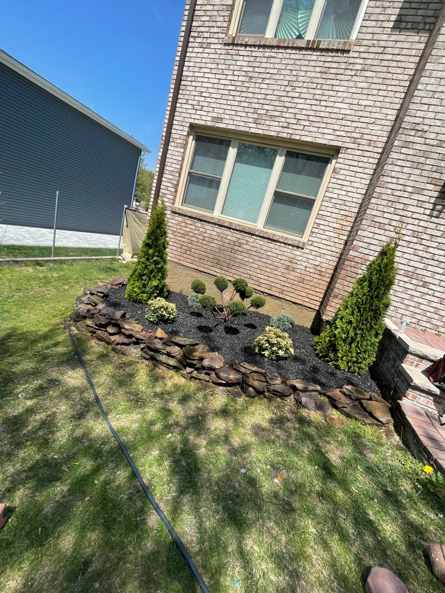 A person is standing in front of a brick house with a garden in front of it.