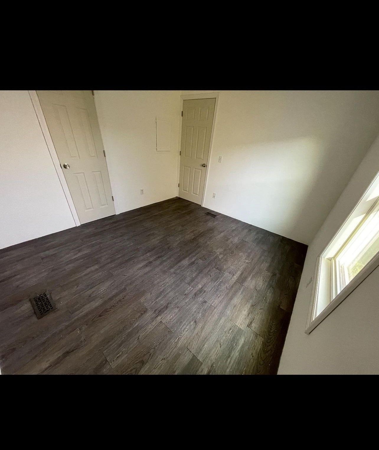 An empty room with hardwood floors and a window.