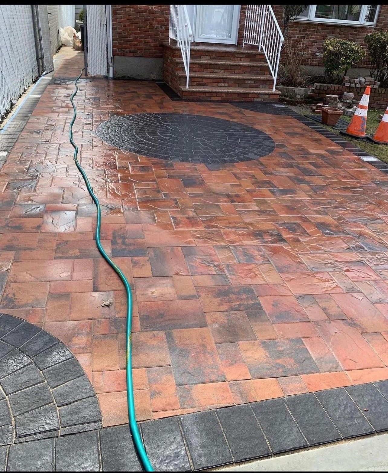 A hose is connected to a brick driveway in front of a house.