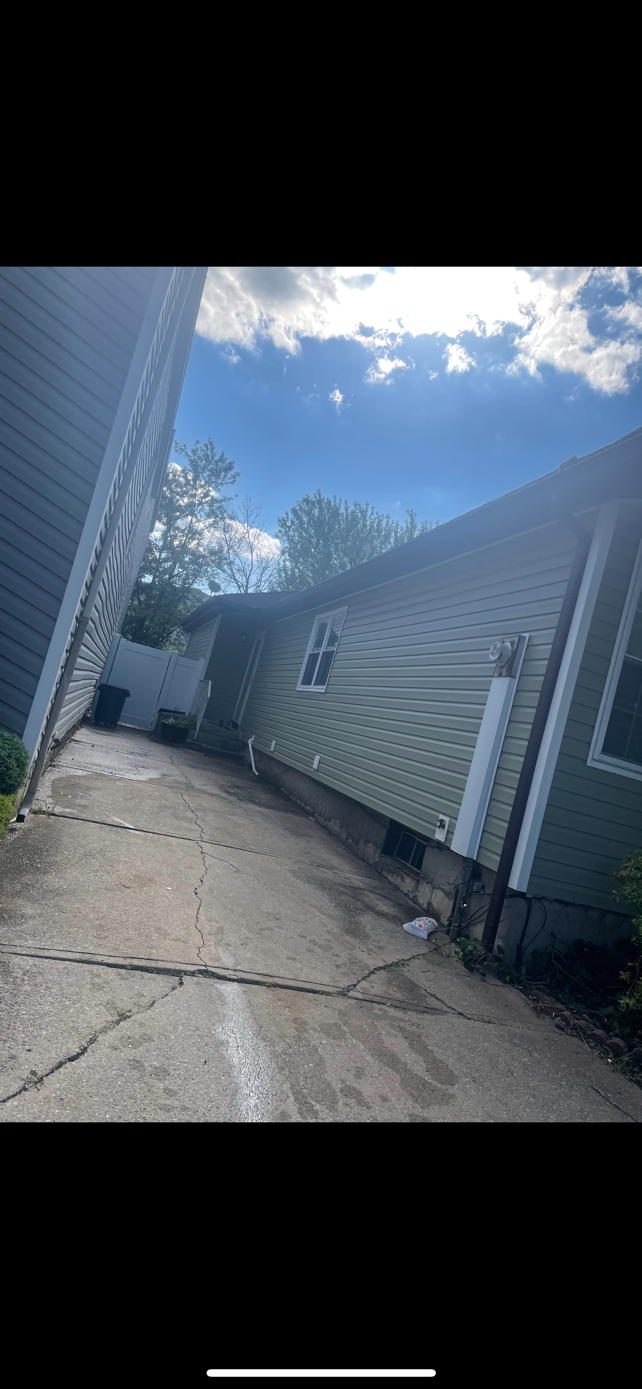 A house with a concrete driveway leading to it and a blue sky in the background.