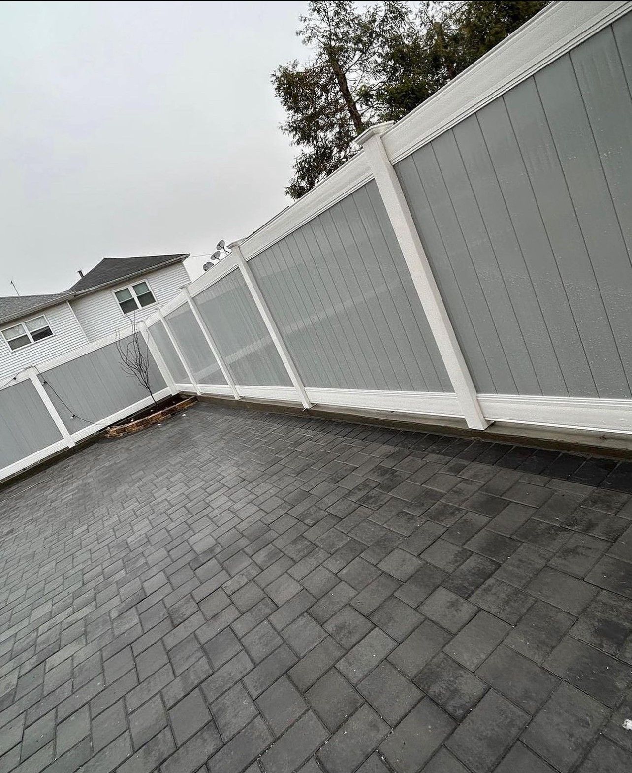 A gray and white fence surrounds a brick driveway.