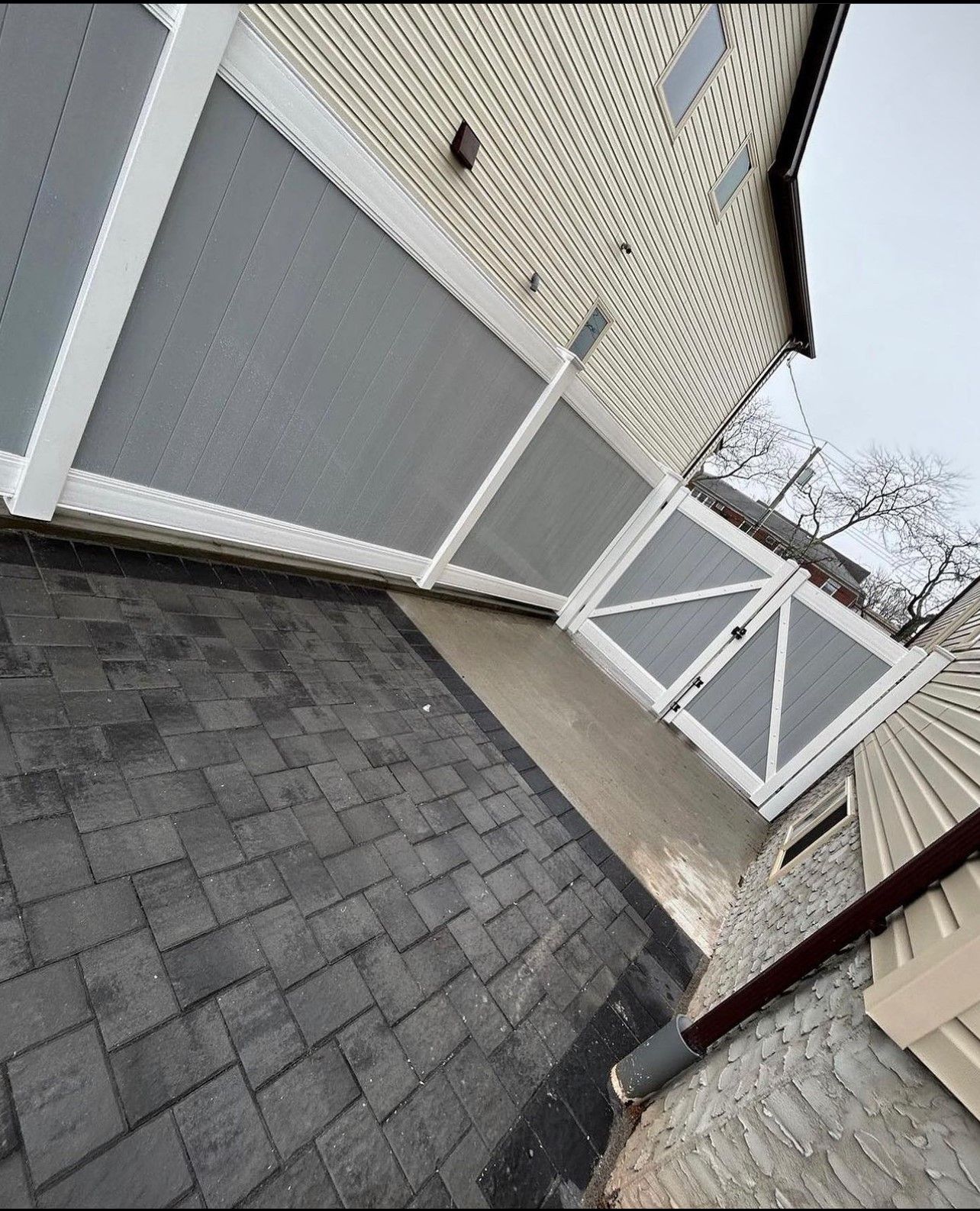 A white fence surrounds a brick walkway next to a house.