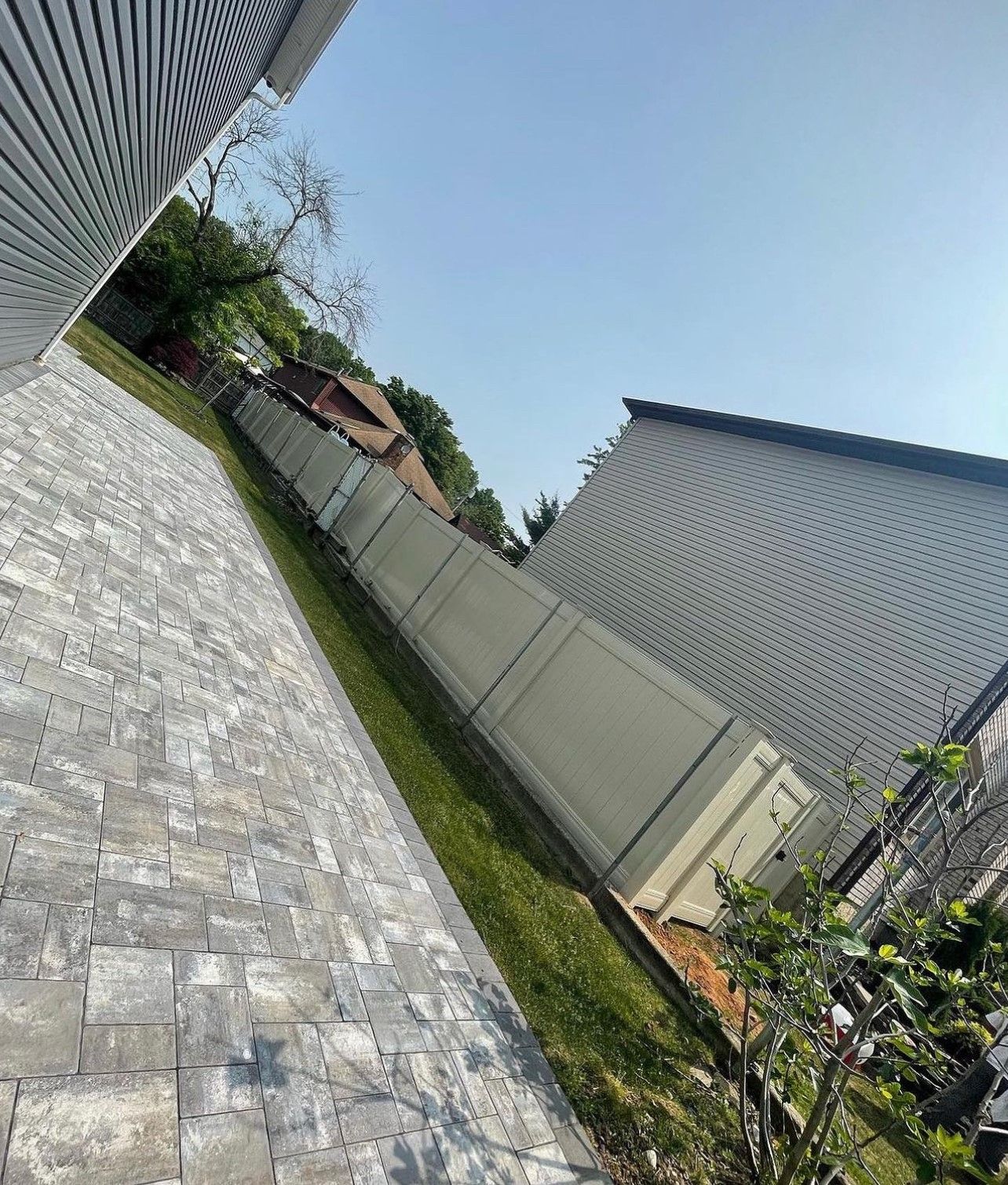 A white vinyl fence is surrounded by a brick walkway and grass.