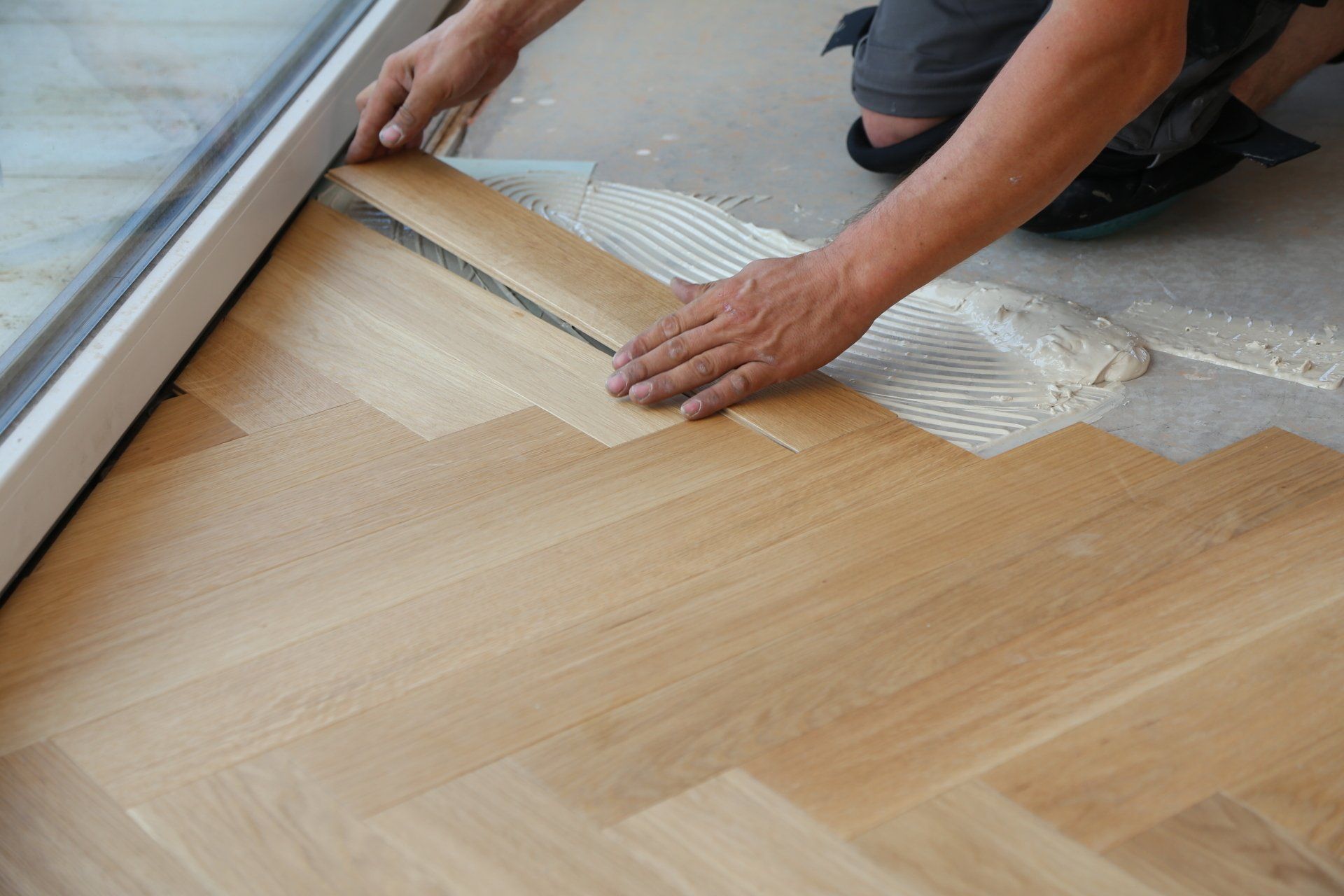 A man is installing a wooden floor next to a window.