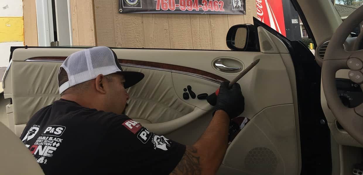 A person in a hat and gloves working on a car door panel with a tool.