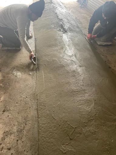 Two men are working on a concrete floor with a trowel.