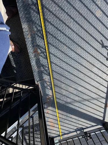 A person is standing on a set of stairs with a yellow tape measure.