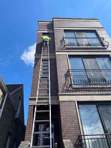 A man is standing on a ladder in front of a tall brick building.