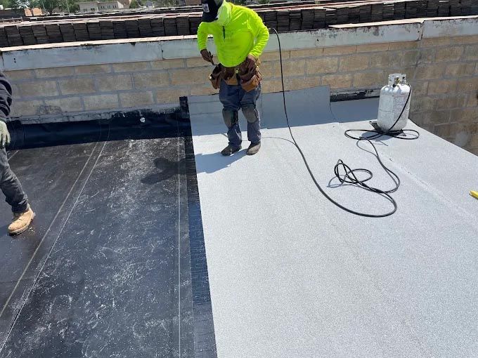 A man is standing on a roof with a propane cylinder next to him.