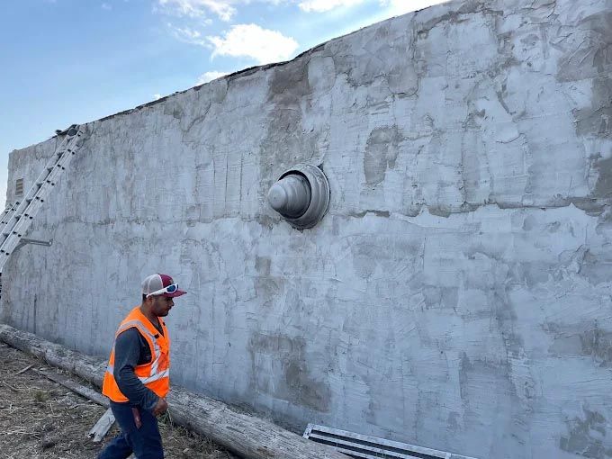 A man in an orange vest is walking in front of a large concrete wall.