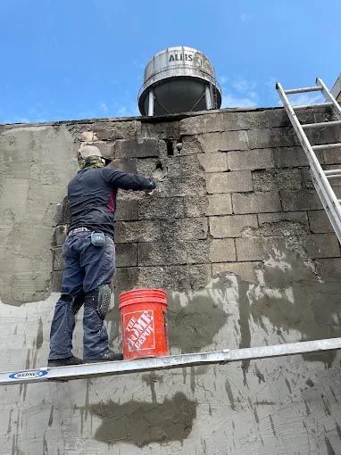 A man is standing on a ledge next to an orange bucket.