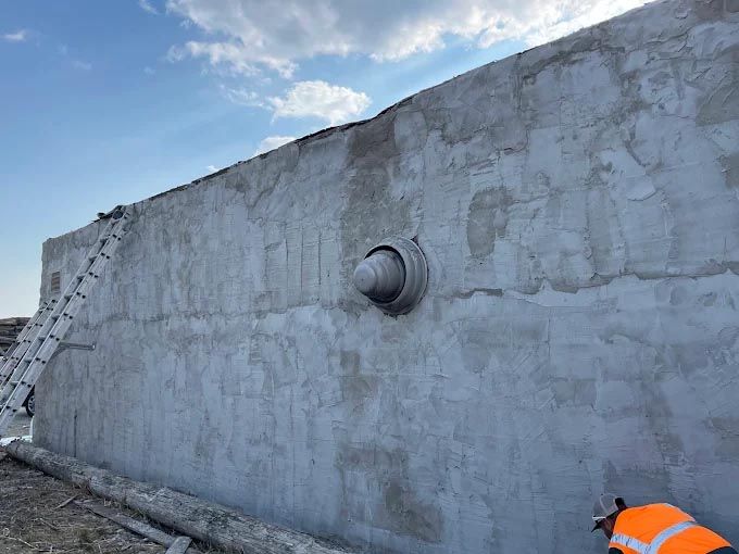 A man in an orange vest is standing next to a large concrete wall.