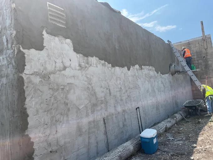 A group of construction workers are working on a large concrete wall.