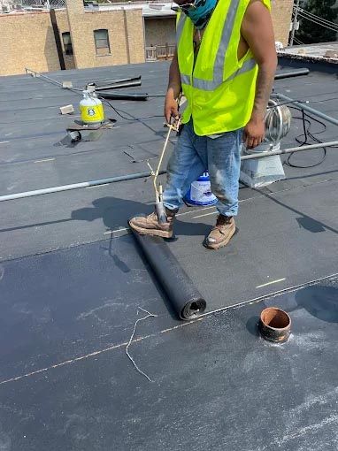 A man in a yellow vest is standing on top of a roof.