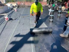 A man is walking on a roof with a roll of roofing material.