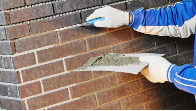 A man is applying mortar to a brick wall with a trowel.
