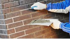 A man is applying mortar to a brick wall with a trowel.