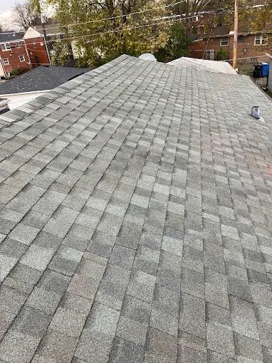 A man is walking on a roof with a roll of roofing material.
