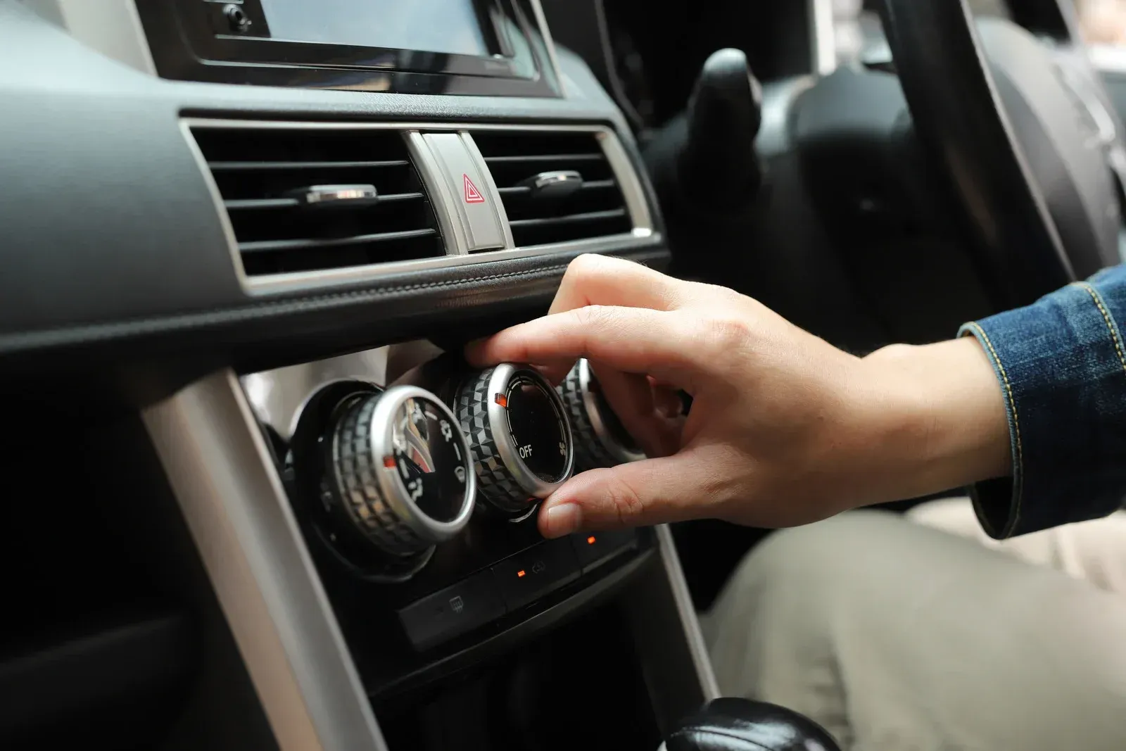 Hand turning a dial on a car's climate control panel.