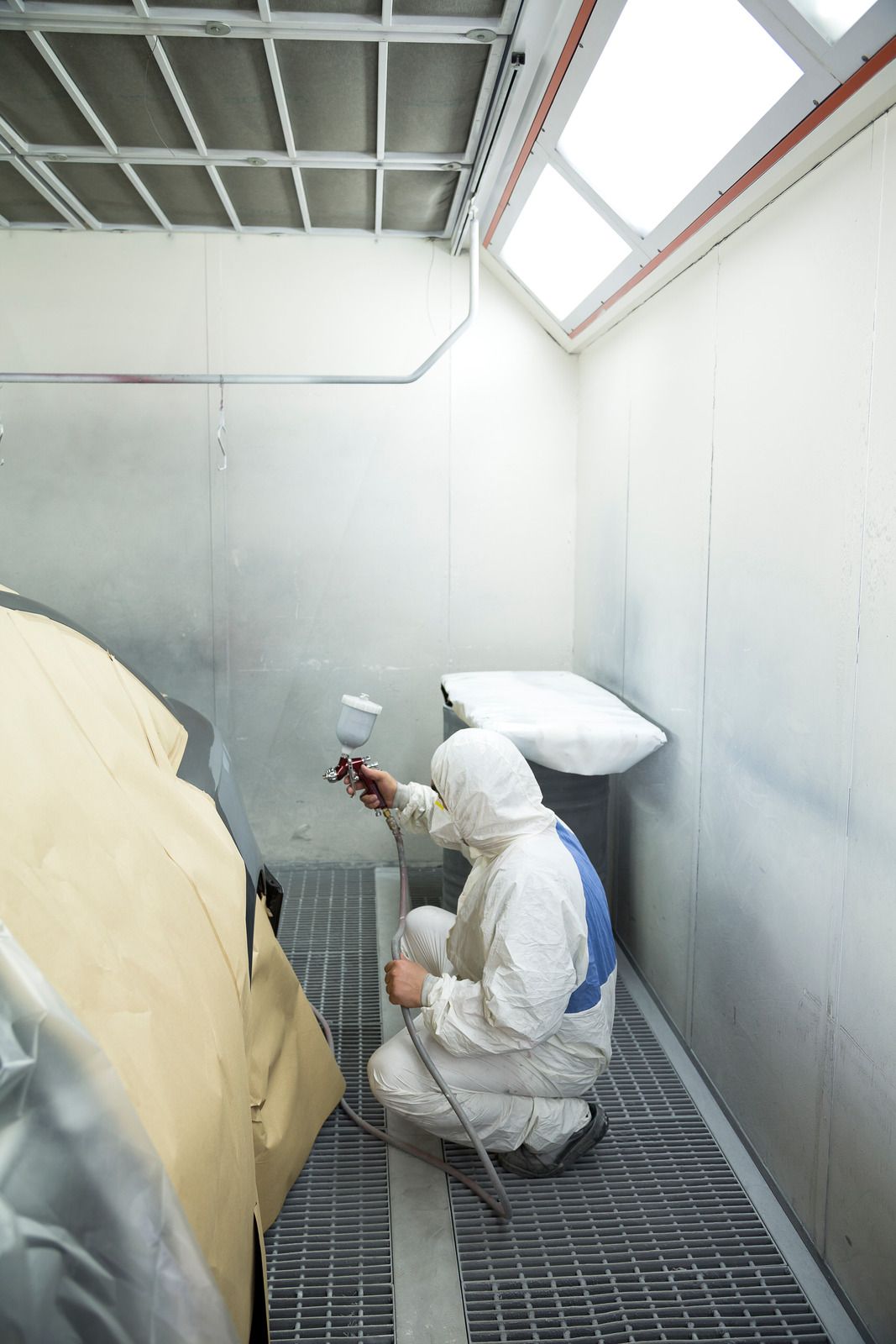 Person in protective suit sprays car part in a spray booth.