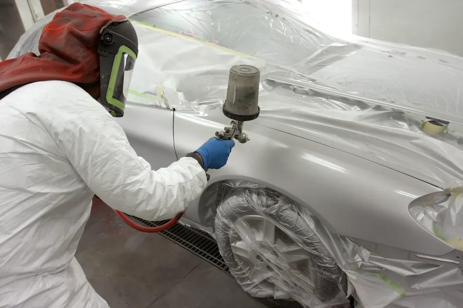 Person in protective suit spraying paint on car in a paint booth.