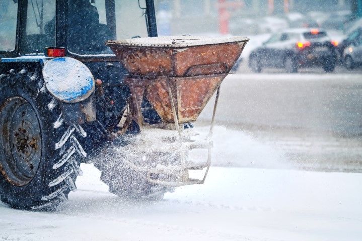 Tractor spreading salt or sand on a snow-covered road in a winter storm