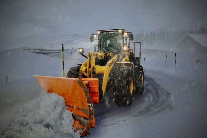 Yellow snowplow clearing a snowy road during a heavy winter storm