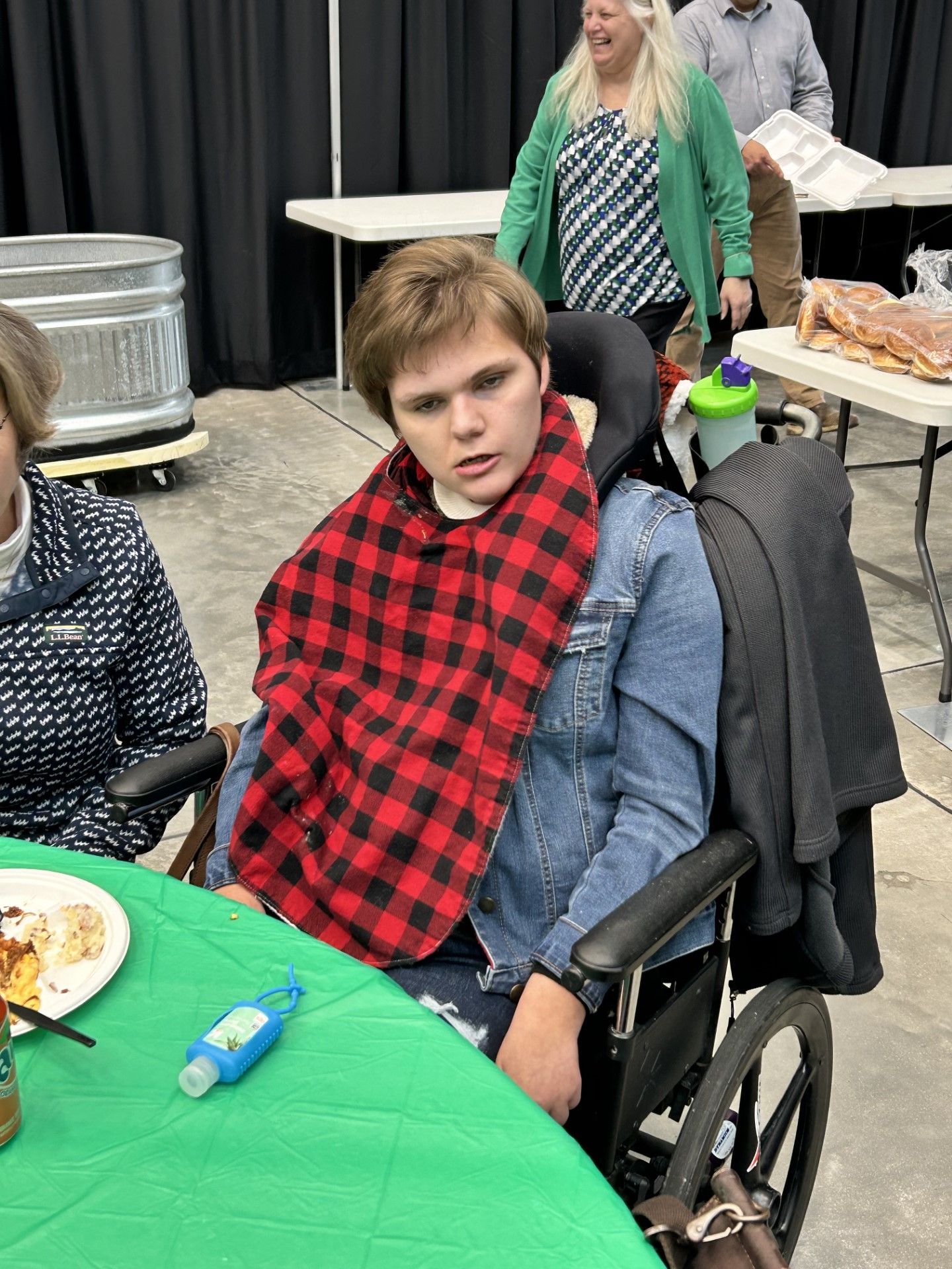 a boy in a wheelchair is sitting at a table with a plaid scarf around his neck .