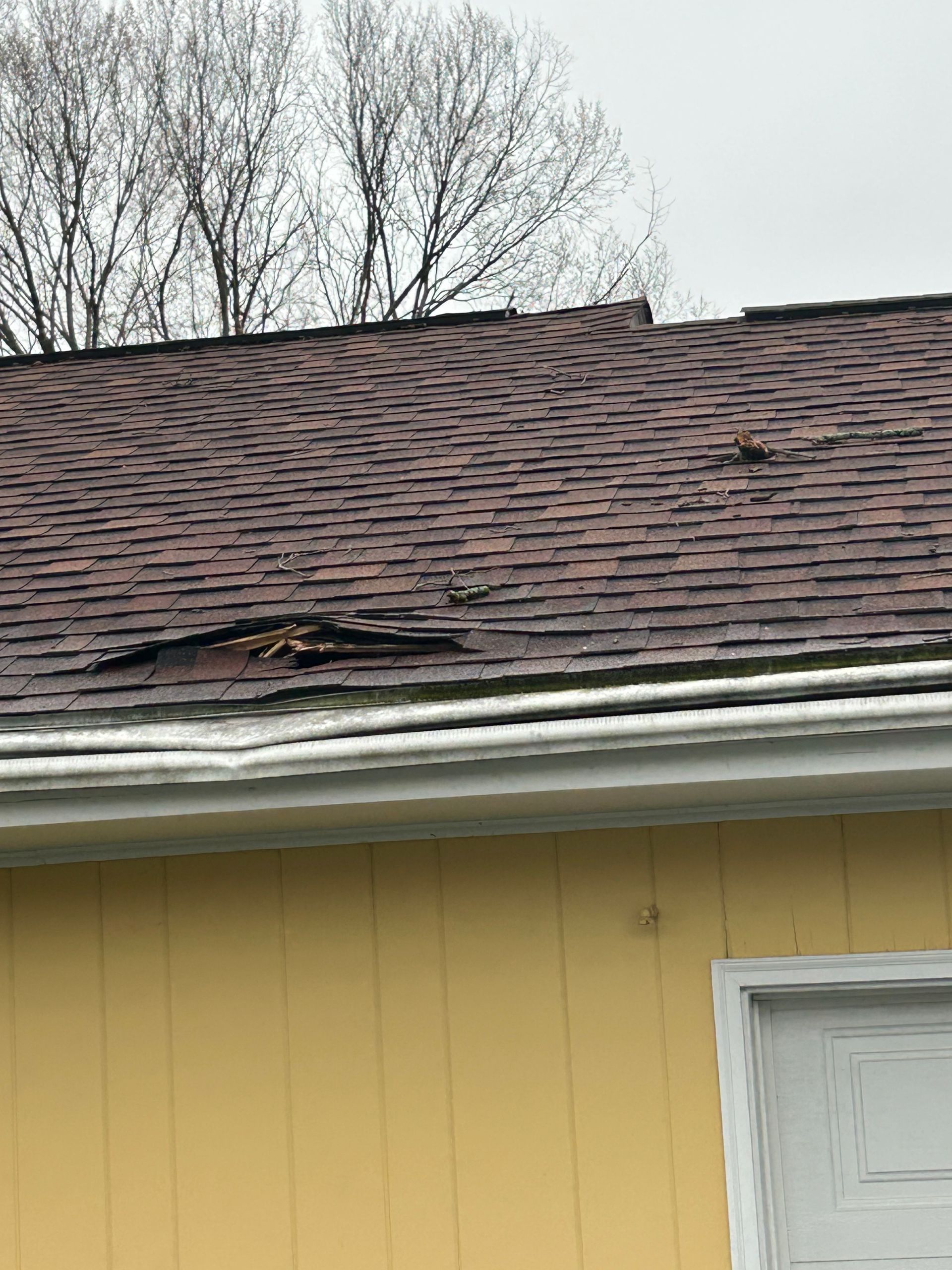 A damaged shingled roof with a section of missing shingles exposing the underlying wooden deck.