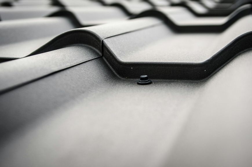 A close-up of dark grey, textured metal roofing panels with a visible fastener.
