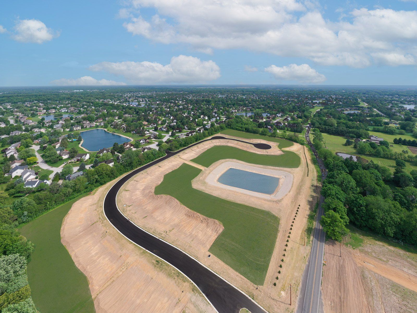 Aerial view of a new housing development under construction near a lake and town, on a sunny day.