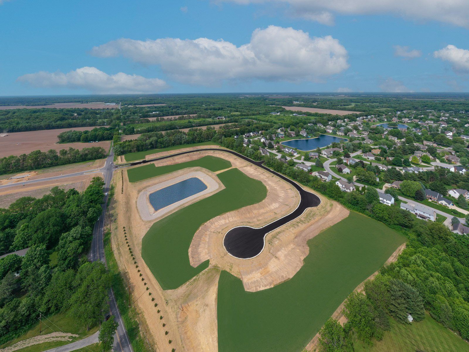 Aerial view of a planned residential development with a lake, roads, and surrounding houses under a blue sky.