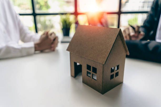 Real estate agent talks to their client in the background, with a wooden model of a house in front.