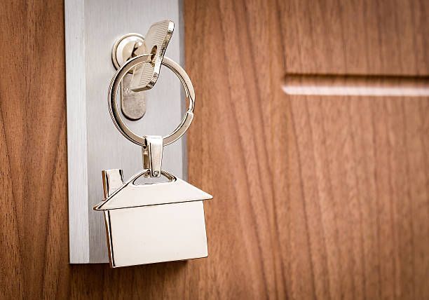 Close-up of a silver key with a house shaped keyring being inserted in a wooden door’s lock.