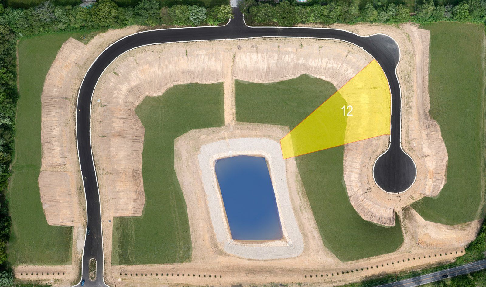 Aerial view of construction site with roads, pond, and a highlighted lot labeled 